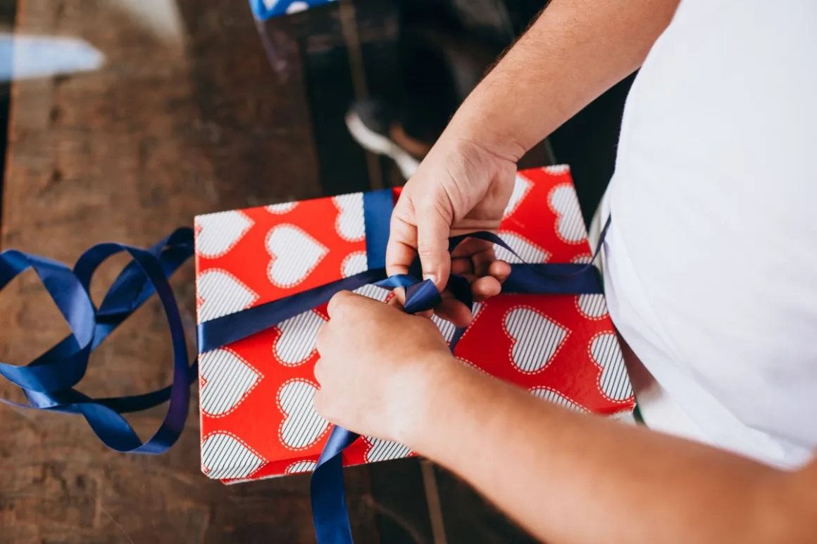 Valentine's Day Gifts: 15 Smart Ideas That Beat Boring Flowers Hands tying a ribbon on a heart-patterned present, one of many Valentine's Day gifts